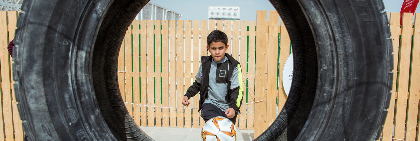 Youth participating in National Sports Day - kicking a soccer ball through a tire.